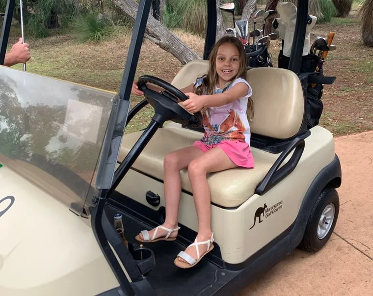 Todd's daughter grinning behind the wheel of a parked golf cart