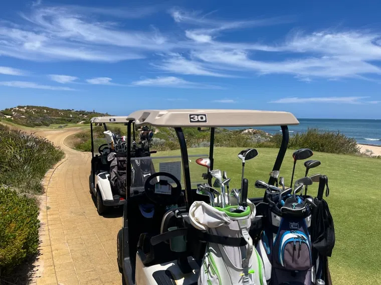 Two golf carts parked on a coastal path, the fairway running along the dunes beside the ocean