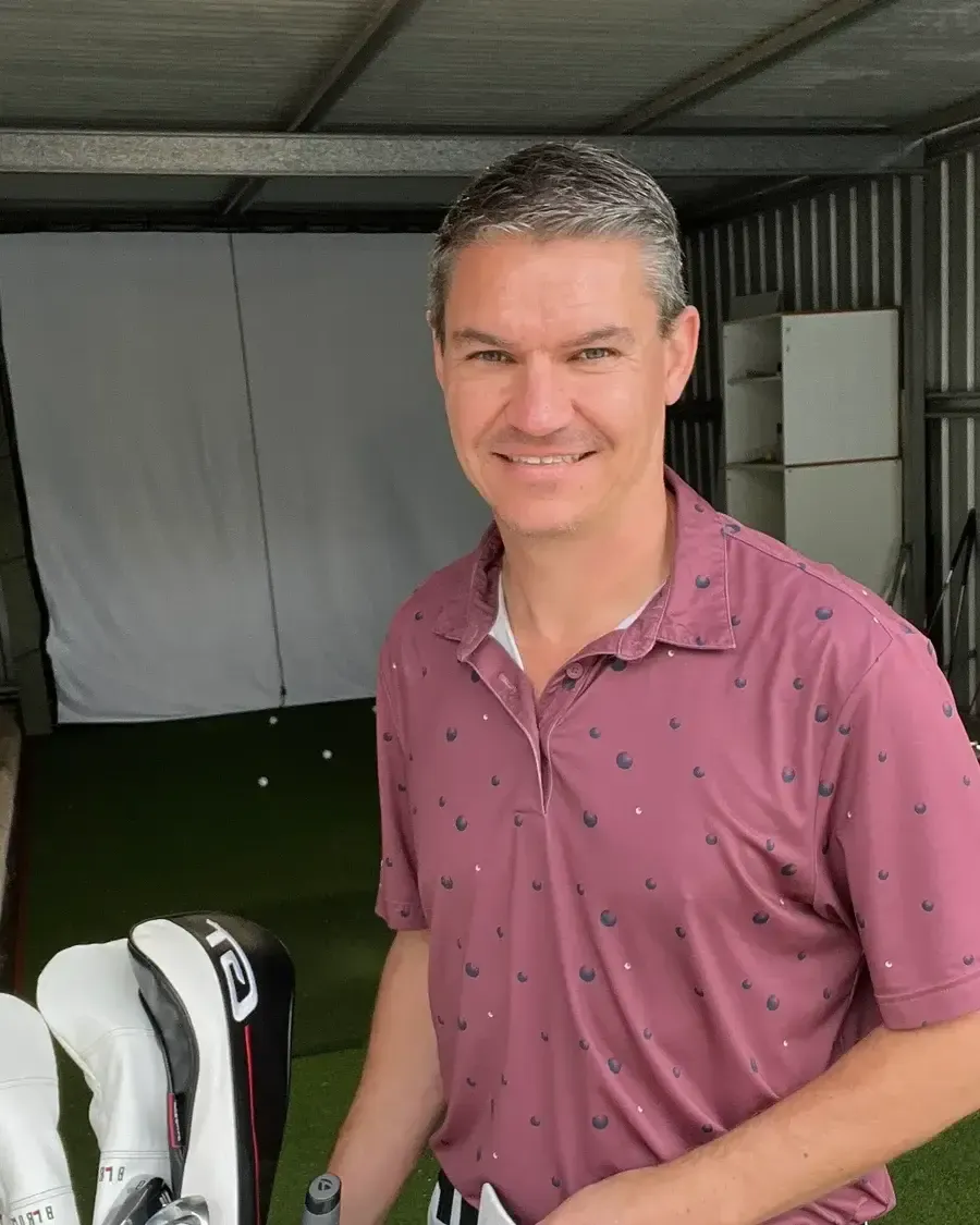 Todd standing beside his golf bag in a practice bay