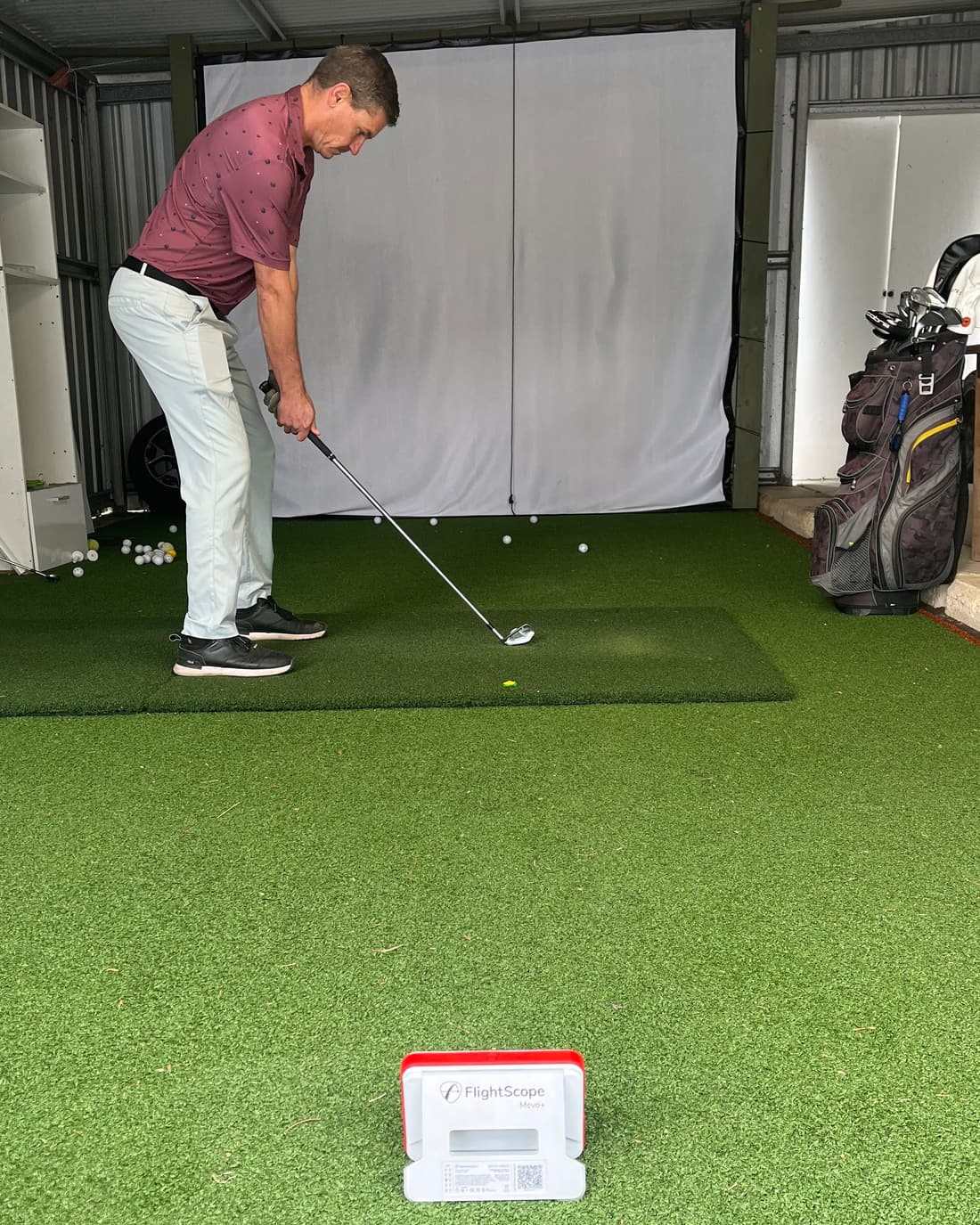 Todd at address with an iron in his home practice bay, hitting into a net with a launch monitor on the turf in front of him
