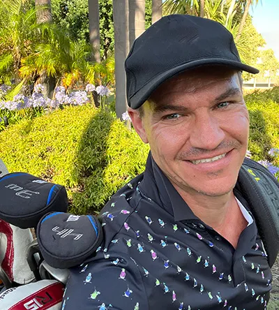 Todd in a cap beside his golf bag before a round