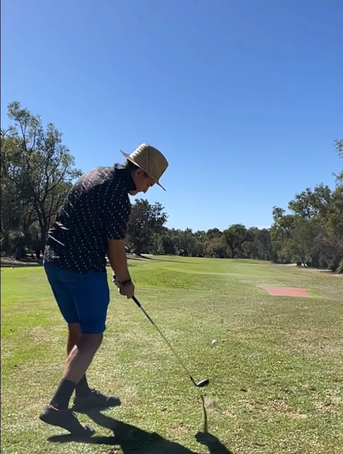 Todd standing over the ball in a straw hat, about to play a shot from the fairway